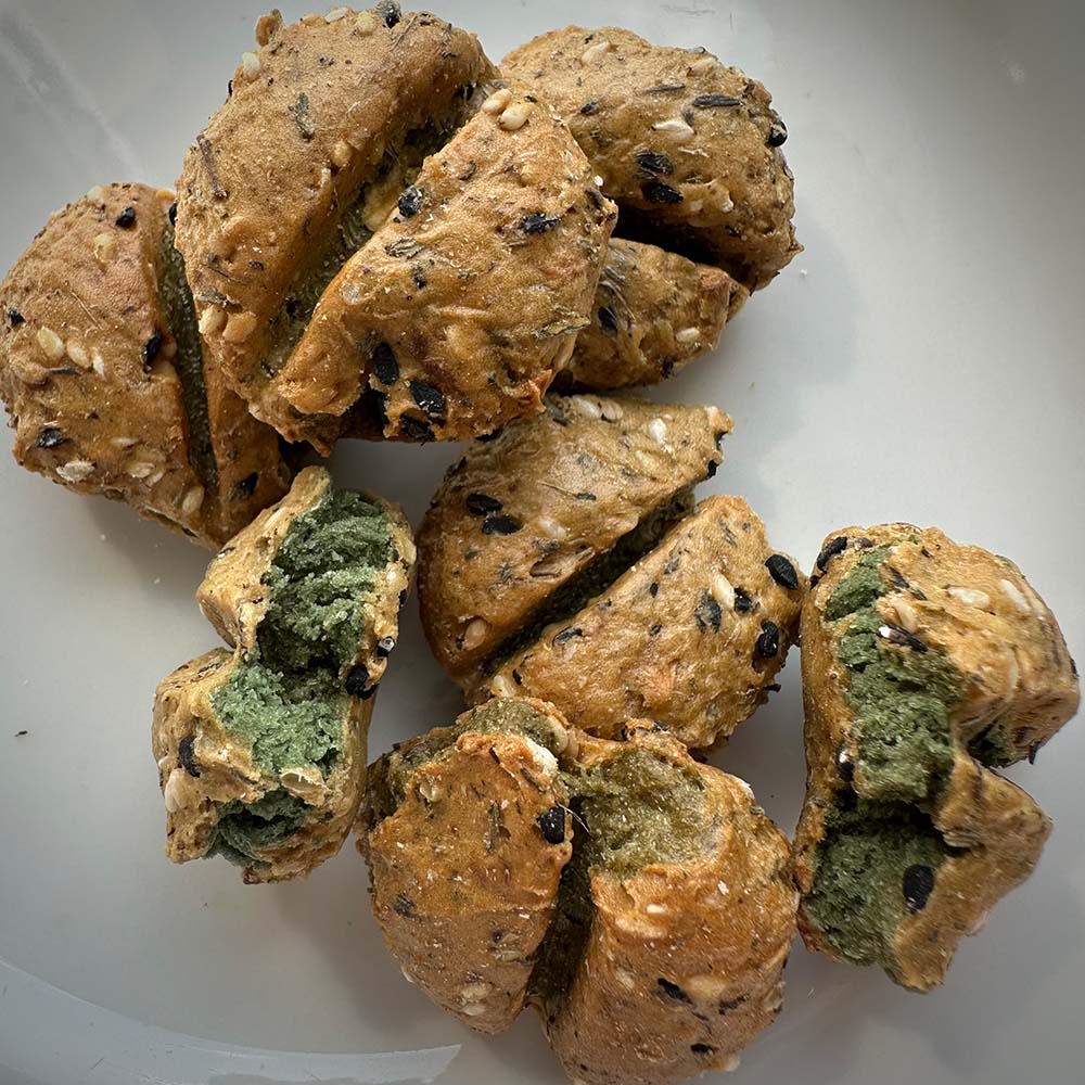 Vegan dog treats Lorelai by Vegan4Dogs: Baked snacks with sesame and black cumin, partially broken open showing a green filling made of spinach, spirulina, and nori flakes.